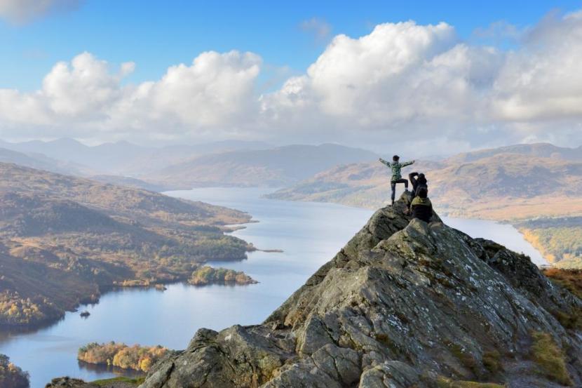 Person standing on top of Ben A'an hill viewing the loch below