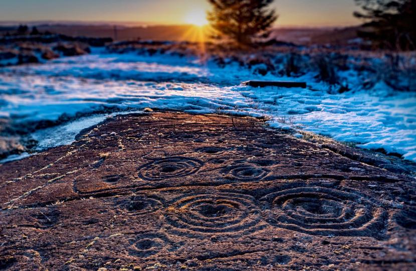 Kilmartin Glen's carved rocks; a sunset and snow scene with concentric circles carved multiple times into the rock.  
