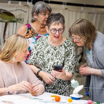A group of volunteer stitchers surrounding Kirstie Campbell, Spirit of the Highlands &amp;amp; Island tapestry stitch co-ordinator