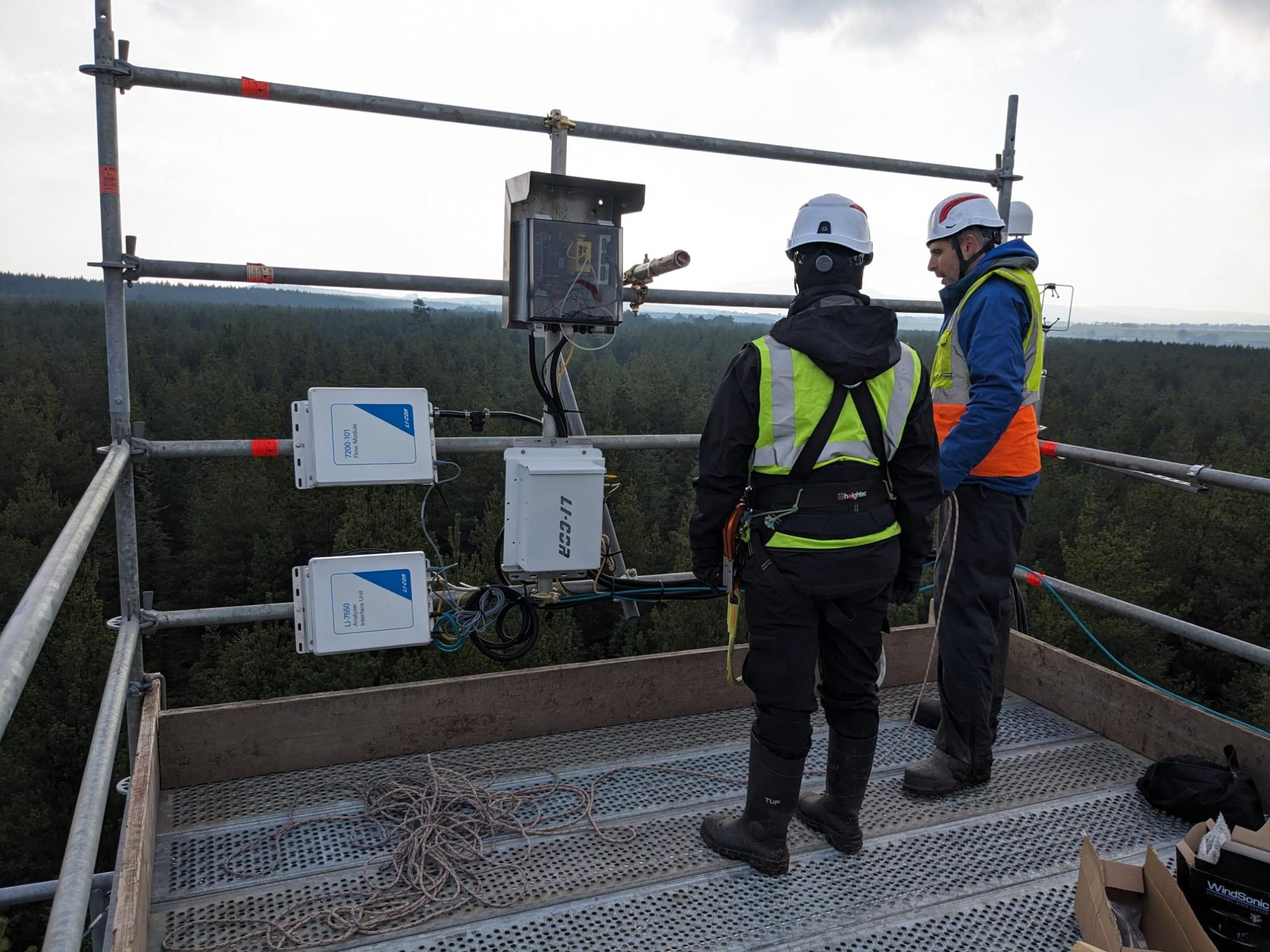 Image showing two people standing gat the top of the flux tower scaffold looking at the monitoring equipment with a view over the plantation.